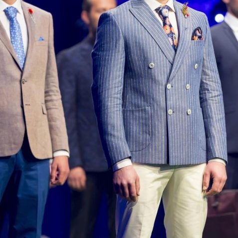 Male models walk the runway in different modern and colourful suits during a Fashion Show. Fashion catwalk event showing new collection of clothes. Vivid colours.