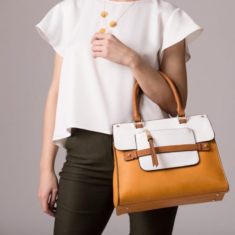 Stylish woman in modern clothes with bright orange white handbag in hands posing at studio isolated on gray background