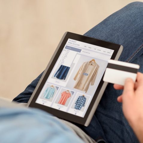 Pay it off. Pleasant man sitting on the couch and holding credit card while using tablet